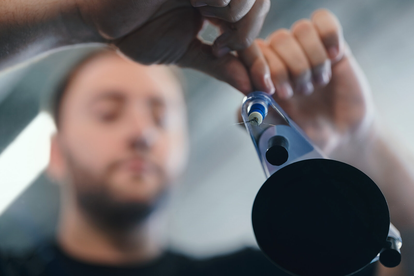Ein Fokus auf eine Person, die eine präzise Technik anwendet, um ein kleines Objekt mit einem durchsichtigen Werkzeug zu befestigen. Der Hintergrund ist unscharf, wodurch die Handlung und das Werkzeug hervorgehoben werden.