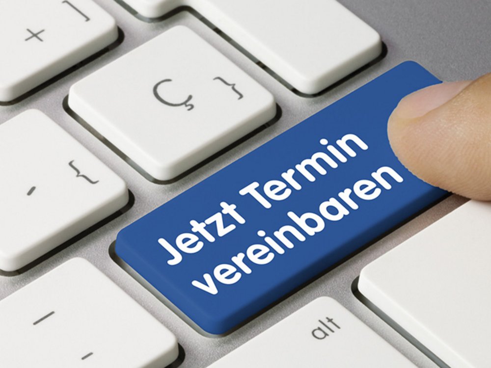 Ein Finger drückt auf eine blau gefärbte Taste einer Computer-Tastatur, auf der Jetzt Termin vereinbaren steht. Die anderen Tasten sind hell und neutral gehalten. Die Taste hebt sich deutlich durch ihre Farbe und den Text hervor.